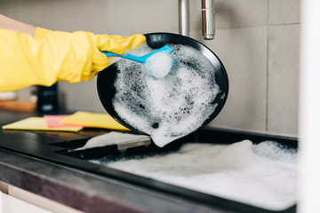 Close up of woman hand in yellow protective rubber gloves washing dishes in the kitchen.