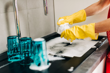 Woman in yellow protective rubber gloves washes dishes in the kitchen..