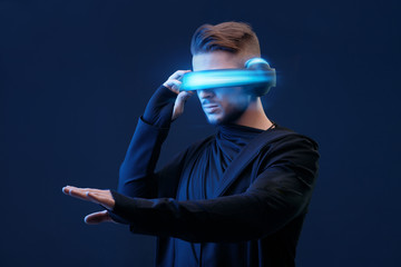 Guy using VR helmet scrolling invisible screen while interacting with virtual reality under neon...