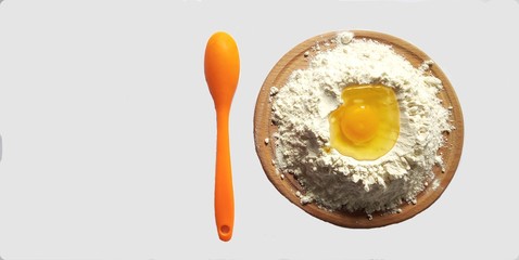 Raw egg in flour on a chopping board an orange spoon on a white background