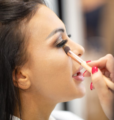 Face of a young girl with makeup and cosmetic brush in the makeup artist’s hand
