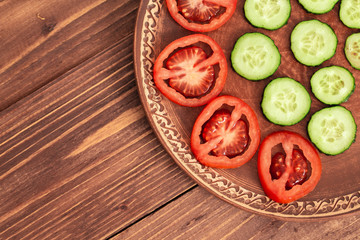 sliced tomatoes and cucumbers in a clay brown plate on a wooden table. top view