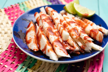Mexican jicama  cutted with chili powder and piquant sauce on turquoise background