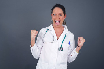 Waist up portrait of strong successful determined young female winner in casual t-shirt raising arms, clenching fists, exclaiming with joy and excitement. Victory, success and achievement concept.