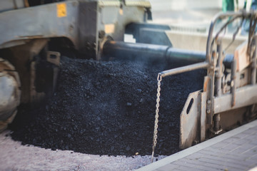 Asphalt paver machine and steam road roller during road construction and repairing works, process of asphalting and paving, workers working on the new road construction site, placing a layer