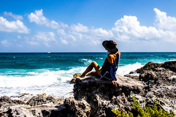 Beautiful, young and sexy woman in bikini sitting on the rocks of the caribbean sea, tropical beach looks at the waves on the horizon, blue and crystal clear sea, paradise and summer time