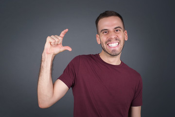 Blond European man over isolated background gesturing with hand showing small size, measure symbol....