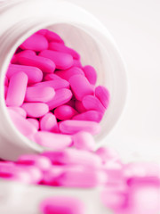 Obraz na płótnie Canvas Purple pills spilled out of a plastic jar. Medicine capsules on white background.