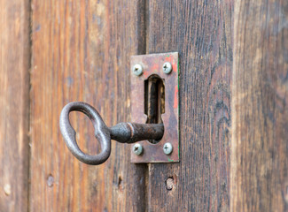 old or vintage key made by metallic iron inside a lock of a wooden door. The old key and the lock...