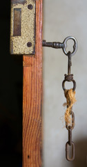 old or vintage key made by metallic iron inside a lock of a wooden door which is opened. The old key and the lock are completely rusty and a string hangs from the key. Vertical photo with nobody.