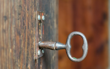 old or vintage key made by metallic iron inside a lock of a wooden door. The old key and the lock are completely rusty and ready to open the door. Horizontal photo with nobody