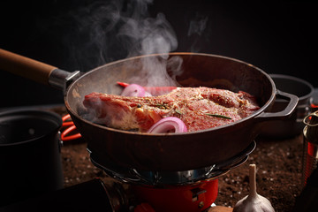 An appetizing piece of meat is fried in a frying pan on a gas hot. Styling for cooking in the field