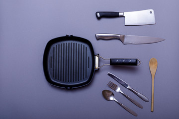 Metal knives with black on a grey table, grill pan, towel. Flat lay, layout with copy space.