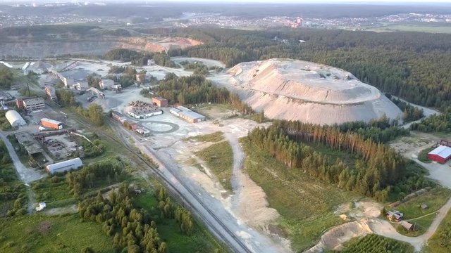 pictorial grey crushed stone barrow at green dense forest against small town under summer setting sun orange light aerial view. Concept old technology