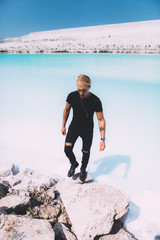 Curly blond man posing at the clear beach. Dressed all black. Awesome background, clear water and sky. Trendy, tropical and attractive man. Summer time
