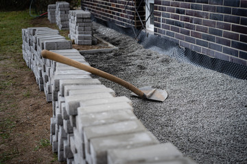Laying gray concrete paving slabs in a house walkway. Stacks of concrete blocks are prepared to be layed on walk or patio on gravel foundation base.