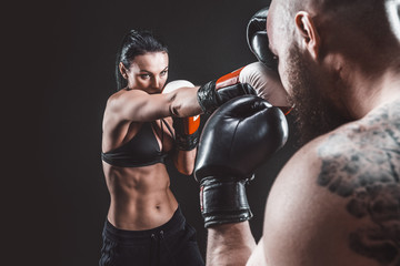 Plakat Shirtless Woman exercising with trainer at boxing and self defense lesson, studio, dark background. Female and male fight.