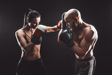 Shirtless Woman exercising with trainer at boxing and self defense lesson, studio, dark background....