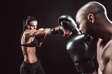 Shirtless Woman exercising with trainer at boxing and self defense lesson, studio, dark background. Female and male fight.