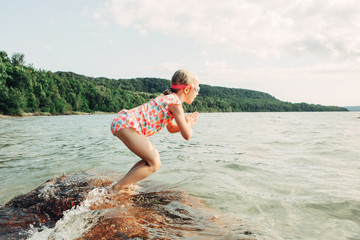 Cute funny Caucasian girl diving in lake with underwater goggles. Child divinswimming in water on a beach. Authentic real lifestyle happy childhood. Summer fun outdoor aquatic seasonal sport activity.