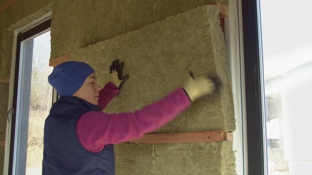 Woman puts a sheet of insulation to the wall with windows of a frame house