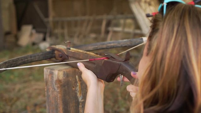Young woman with manicure aims and shoots with a crossbow at open air amusement park