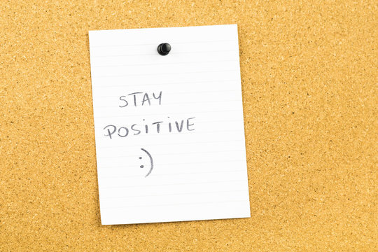Stay positive text on white notebook paper sheet hanging on cork card board. Motivating business background