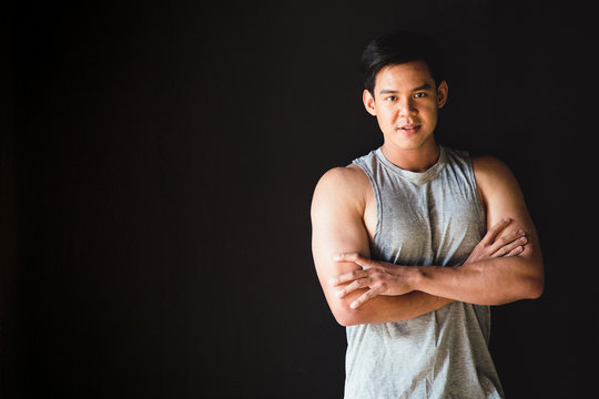 Portrait of a young Asian male sexy model standing in an arms crossed to photograph in a studio with a black background.A man wearing a gray undershirt shows off his muscular arms.