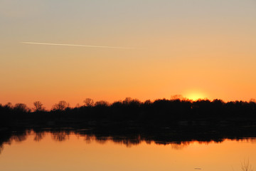 orange sunset behind the forest over the river in early spring