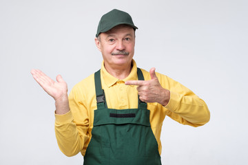 Smiling senior worker looking at camera and pointing aside with index finger. Studio shot