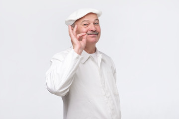 Cooking, food, profession and gesture concept. Smiling senior male chef showing sign ok. Professional male chef in white uniform gesturing excellent. Studio shot