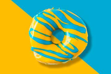Colorful bright yellow and blue glazed  appetizing doughnut on split color background. Top view of...