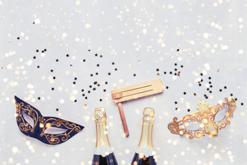 Two champagne bottles, carnival mask and gragger on light background. Flat lay of Purim Carnival...