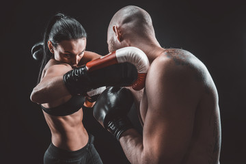 Shirtless Woman exercising with trainer at boxing and self defense lesson, studio, dark background....