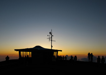 Sunrise behind the Summit Building on Haleakala Summit, with silhouetted people watching, and an...