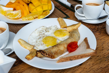 Tropical breakfast of fruit, coffee and scrambled eggs and banana pancake for two on the beach near sea. Top view, table setting.