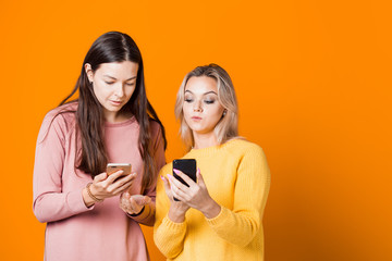 Blonde and brunette with their smartphones on a bright yellow background.