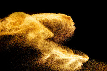Golden sand explosion isolated on black background. Abstract sand cloud.Sandy fly wave in the air.