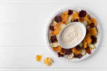 Crisp crunchy organic vegetable chips with oven-baked pumpkin, beetroot, tomato, carrot chips snacks with sauce on a white wooden table