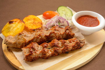Kebab with fried potatoes, onion and vegetables on a wooden board.