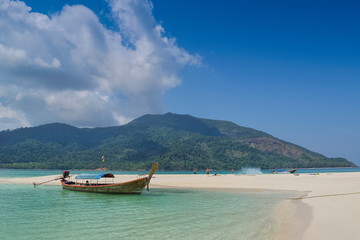 view seaside of a long-tail boat floating in blue-green sea around with white sand beach, green mountain and blue sky background, Lipe island, Satun, southern Thailand.