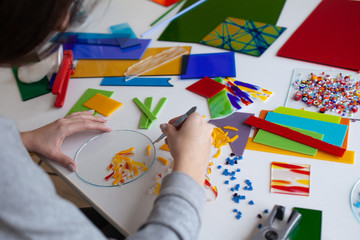 Woman puts out a mosaic of glass with tweezers, fusing, crafting