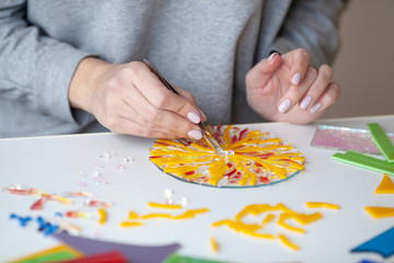 Woman puts out a mosaic of glass with tweezers, fusing, crafting