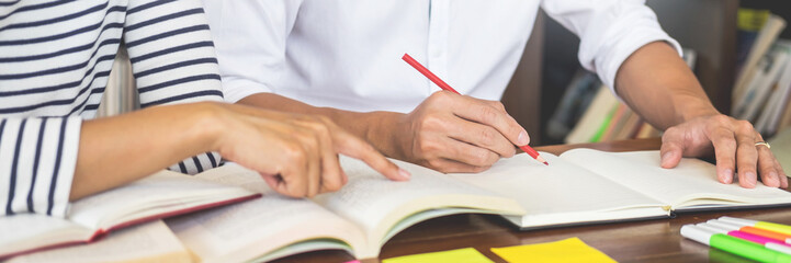 Young students classmates help friend catching up workbook and learning tutoring in a library, education and school concept