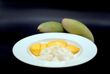 slice ripe mango with sticky rice topped with coconut milk and golden beans on white plate the popular thai dessert in the summer season decorated with two green mangoes isolated on dark background