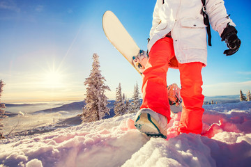 Woman holding snowboard in hands takes step forward. Snowboarding action concept, sunset light