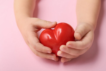 Child's hands with red heart on color background. Cardiology concept
