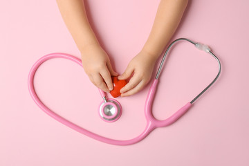 Child's hands with red heart and stethoscope on color background. Cardiology concept