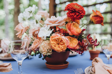 festive tables with tablecloths made of textiles are decorated with flower arrangements, on the tables are candles, plates with napkins, glasses, cutlery, a wedding in the forest, banquet, holiday