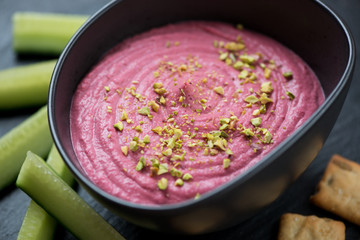 Bowl of beetroot hummus with cucumber slices and crackers, selective focus, close-up